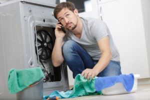 Younger man looking at dryer unit and calling for repairs