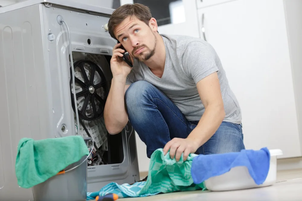 Younger man looking at dryer unit and calling for repairs