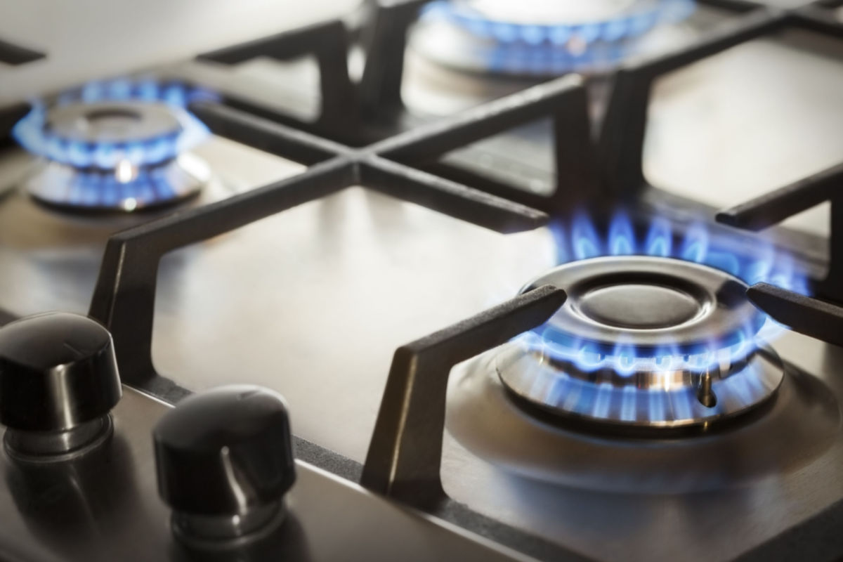 Lit gas stovetop with blue flames and jammed knobs.