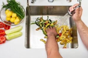 A man washing vegetable peels in a sink.