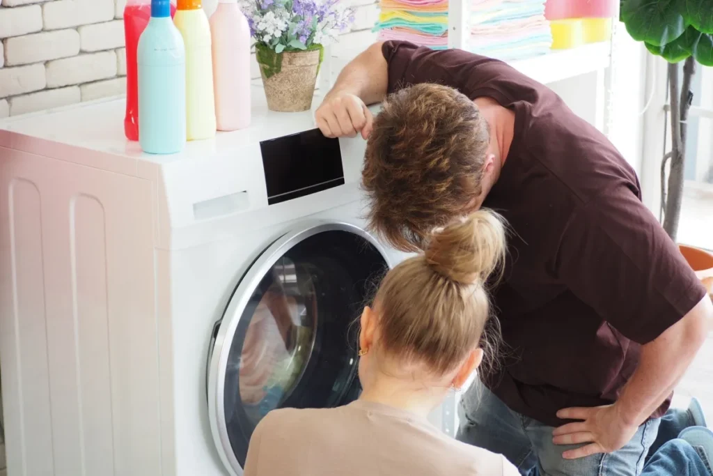 husband and wife leaning over washing machine because the drum isn't spinning