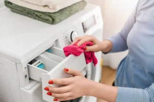 a woman's hand holding a pink rag as she wipes down the detergent dispenser on the washing machine