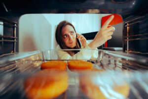 a woman peering into her oven while on the phone with a repairman because her oven isn't heating