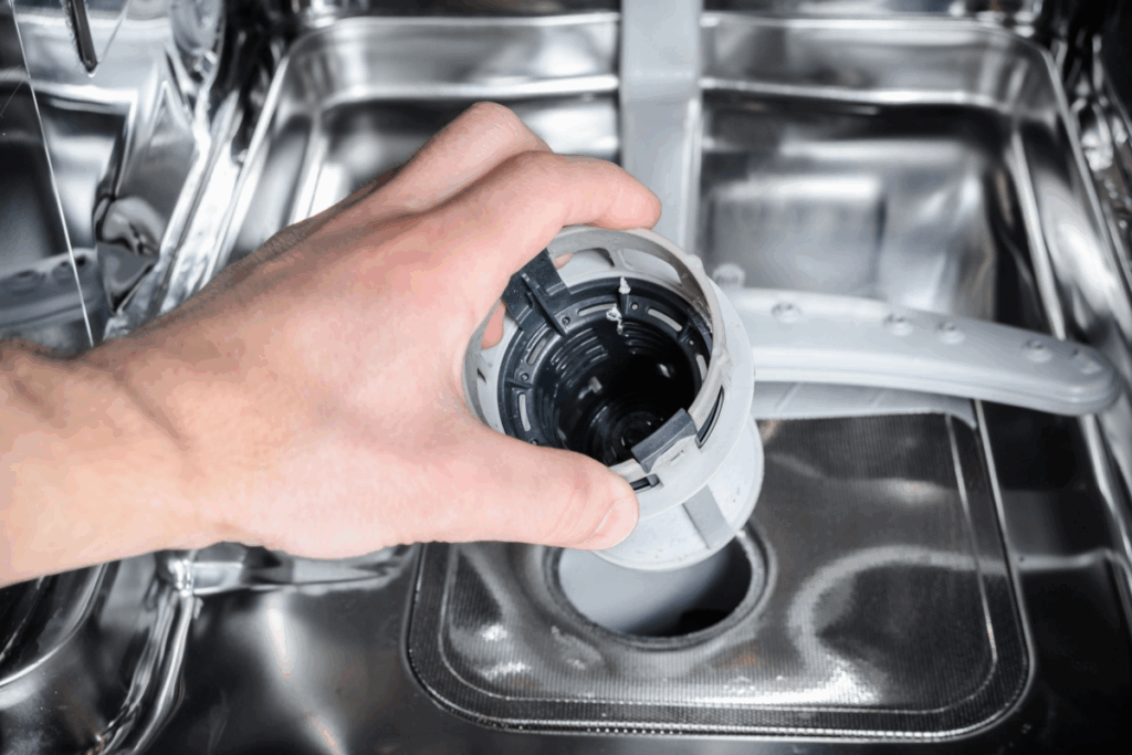 a man's hand pulling the filter from the bottom of the dishwasher