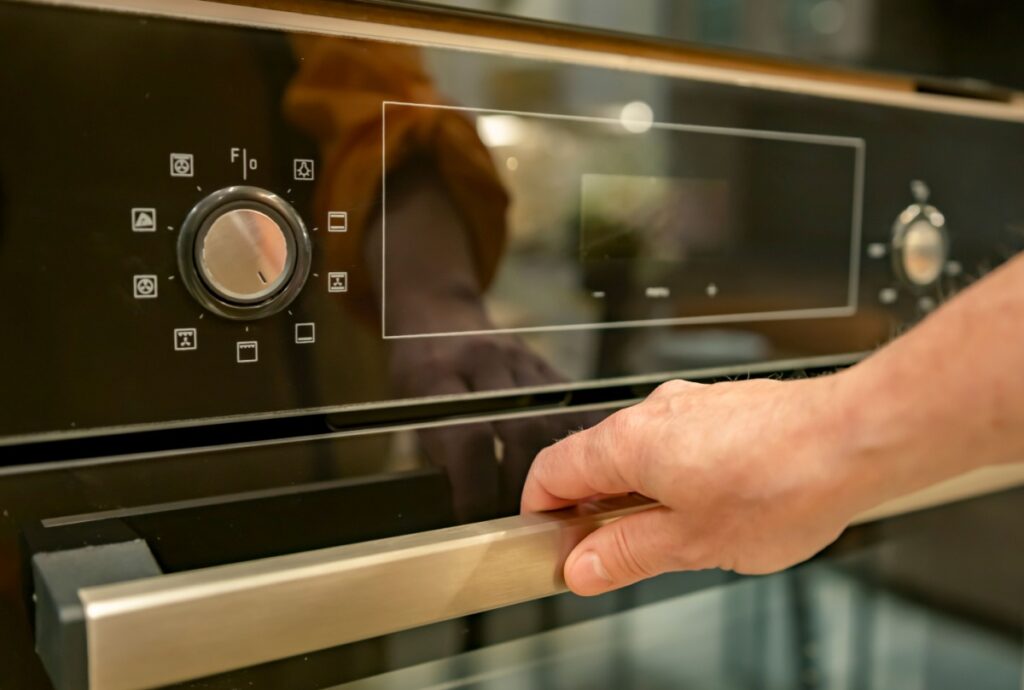 a close-up of a man's hand holding the handle of the oven door and the oven display that is blank