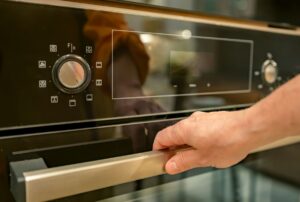 a close-up of a man's hand holding the handle of the oven door and the oven display that is blank