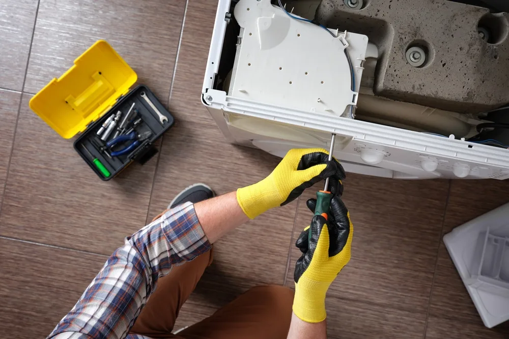 a professional appliance technician fixing a front-loading washing machine with the top panel removed