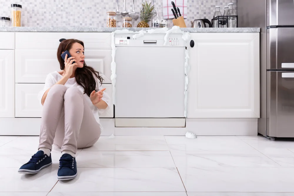 a woman on the phone with a technician as her dishwasher overflows because of bad DIY appliance repairs