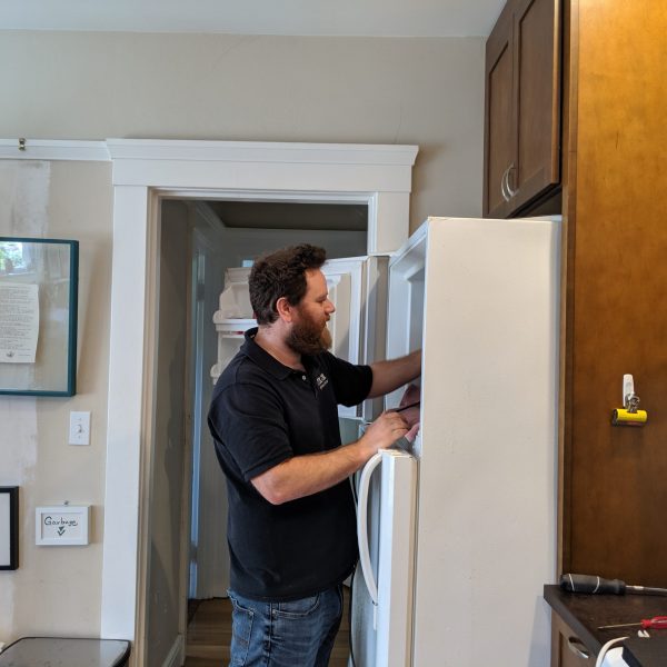 A technician inspecting a refrigerator inside a kitchen.